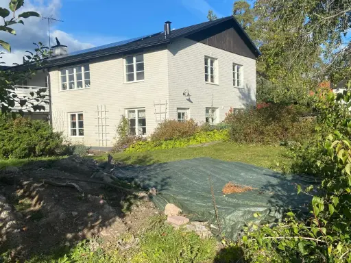 Vitt hus med mörk tak och trädgård. En presenning täcker en del av trädgården, kanske ett gömt hus skatt?
