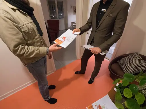 En mäklare ger en broschyr om bostäder till en kund. Kanske handlar det om en kontantinsats på 5 procent.