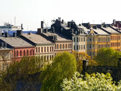 Färgglada husfasader i stadsmiljö, med träd i förgrunden. En vy som kan ge en känsla av belåning per kvadratmeter i en levande stad.