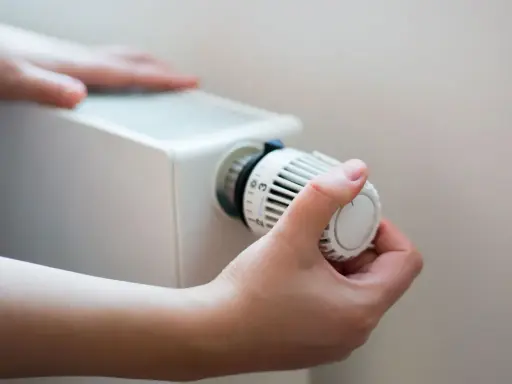 En hand vrider på termostaten till ett vattenburet element för att justera värmen.