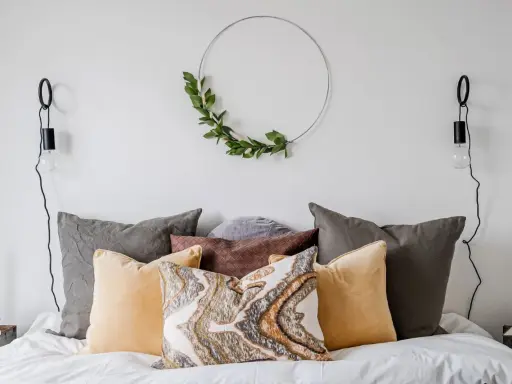 Sovrum inspiration med en säng fylld av kuddar i olika färger och texturer, en grön krans på väggen och minimalistiska vägglampor.