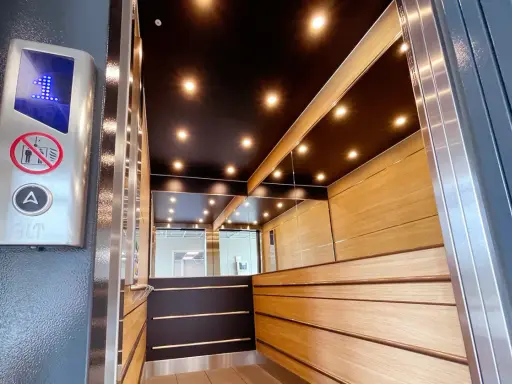 Insidan av en modern, men ändå gammal hiss, med träpaneler, speglade väggar och en svart tak med spotlights. En knapp med siffran 1 lyser.