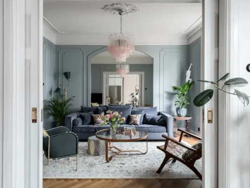 Ett elegant vardagsrum med blåa väggar, en mörkblå soffa, en rosa kristallkrona och en vacker matta. Perfekt vardagsrum inspiration för ett stilfullt hem.