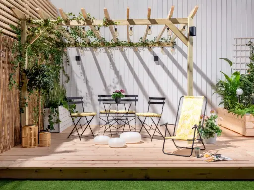 En mysig uteplats med träpergola, belysning och sittgrupp. Buskar insynsskydd ger avskildhet.