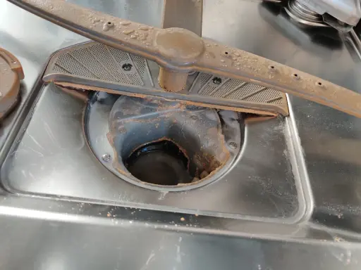 Diskmaskinens filter och spolarm är smutsiga, med matrester och kalkavlagringar. Det är tydligt att man måste ha salt i diskmaskinen för att undvika detta.