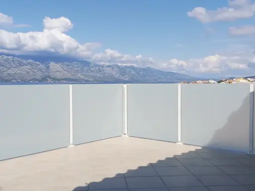 Frosted glass privacy screens on a tiled patio with a view of mountains and the sea.
