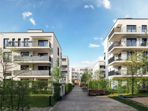 Moderna bostadshus med balkonger och grönska. En lugn innergård med gångväg, bänk och cyklar. Perfekt för en trygg boendemiljö, som en revisor brf skulle uppskatta.