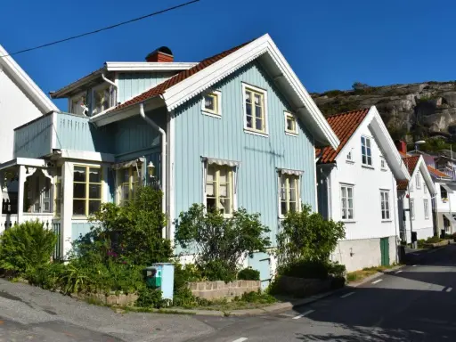 Blå och vita trähus längs en gata, med klippor i bakgrunden. Undrar hur mycket fastighetsskatt dessa vackra hus har.