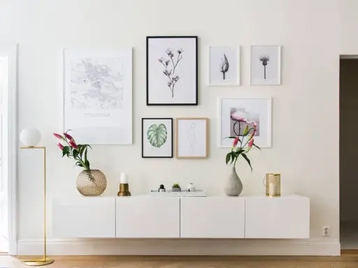 Ett modernt, inrett avlastningsbord med konstverk och blommor. En vit skänk med en guldig lampa, vaser och ljus.