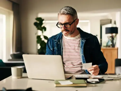Man med glasögon kollar papper och laptop, kanske för att se vad kollar banken vid bolån.