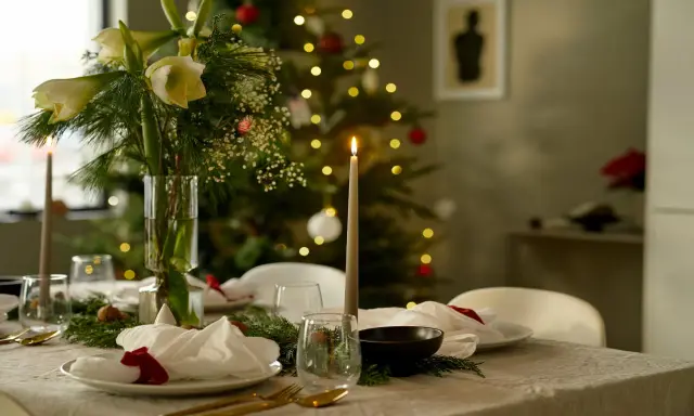 Vacker julpynt inspiration med dukat bord, amaryllis och julgran i bakgrunden. Ljusen skapar en mysig stämning.