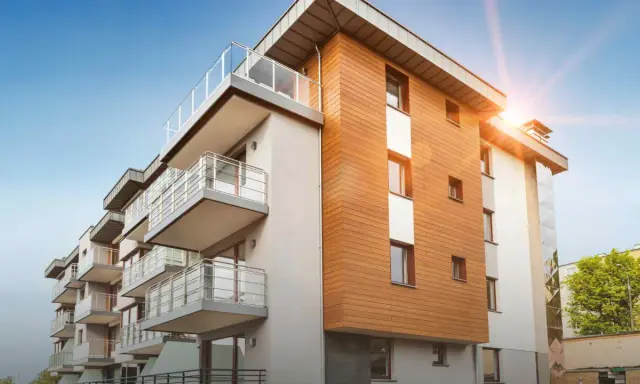 Modernt bostadshus med träfasad och balkonger. Solen skiner, en bild av trygghet och ansvarsfrihet för styrelse.