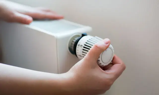 En hand vrider på termostaten till ett vattenburet element för att justera värmen.