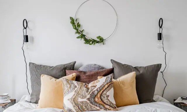 Sovrum inspiration med en säng fylld av kuddar i olika färger och texturer, en grön krans på väggen och minimalistiska vägglampor.