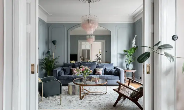 Ett elegant vardagsrum med blåa väggar, en mörkblå soffa, en rosa kristallkrona och en vacker matta. Perfekt vardagsrum inspiration för ett stilfullt hem.