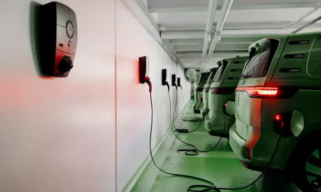 Rad med gröna elbilar laddas vid laddstolpar. Systemet för debitering laddstolpar är igång, vilket syns på de röda lamporna.