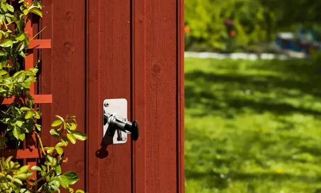 Ny vattenutkastare monterad på rött trä. En klätterväxt slingrar sig på vänster sida.