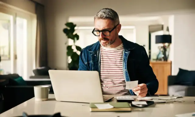 Man med glasögon kollar papper och laptop, kanske för att se vad kollar banken vid bolån.