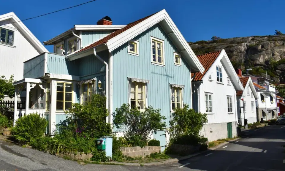 Blå och vita trähus längs en gata, med klippor i bakgrunden. Undrar hur mycket fastighetsskatt dessa vackra hus har.