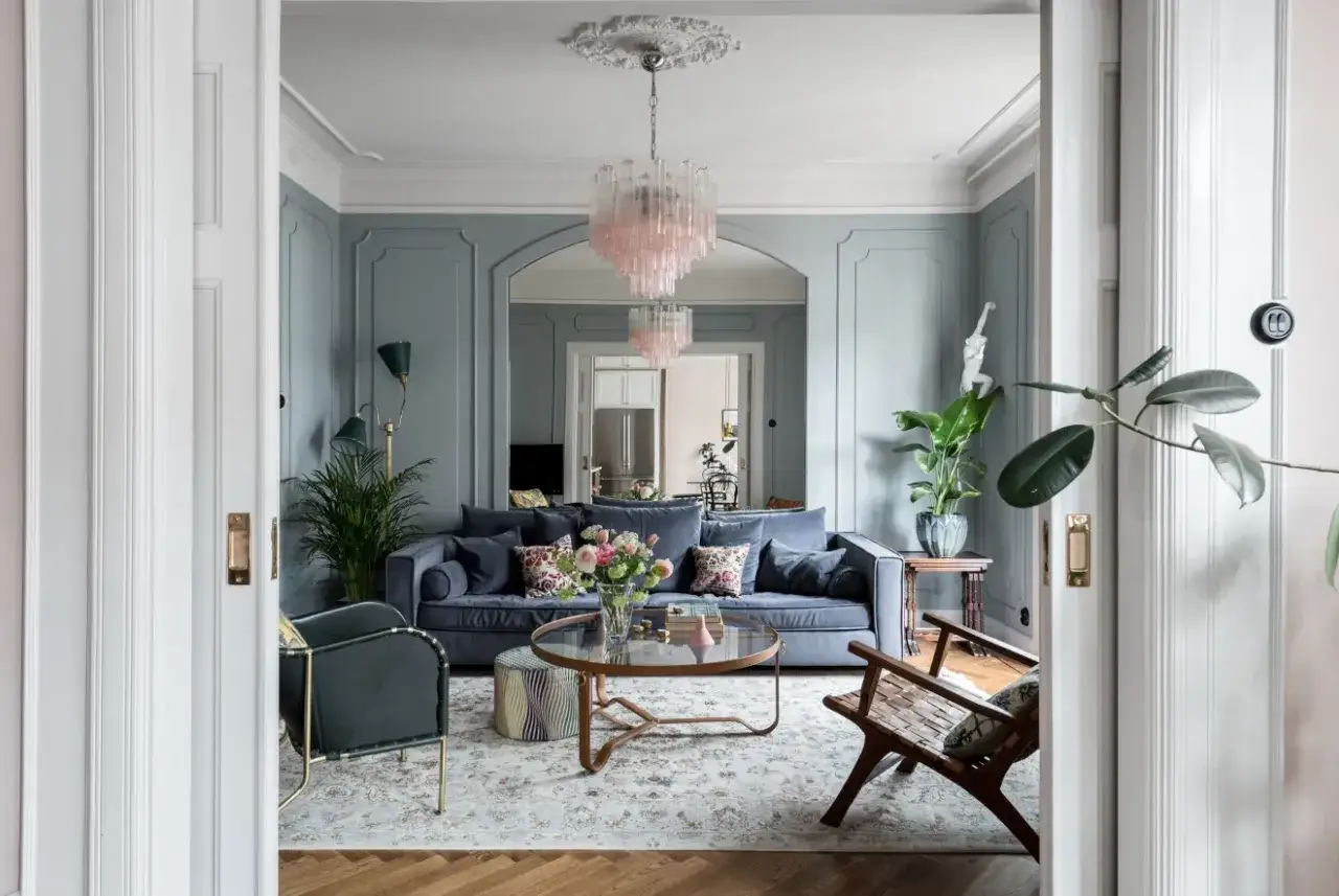 Ett elegant vardagsrum med bl&aring;a v&auml;ggar, en m&ouml;rkbl&aring; soffa, rosa taklampor och en vacker matta. Perfekt vardagsrum inspiration f&ouml;r ett stilfullt hem.