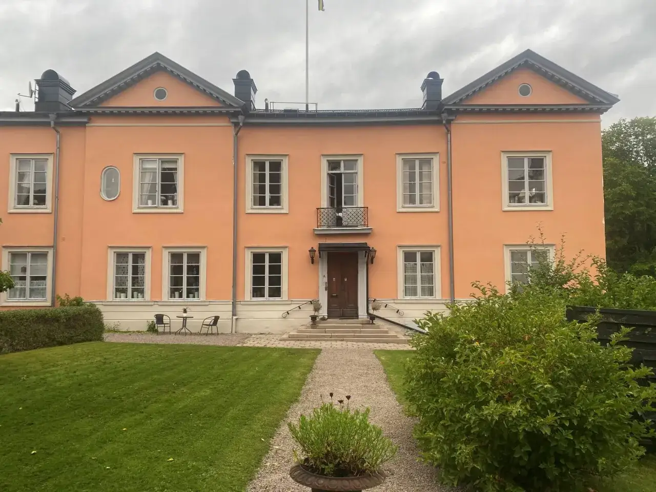 Ett persikofärgat hus med många fönster och en vacker trädgård. Kanske en plats för gemensamma medlemsinsatser brf.
