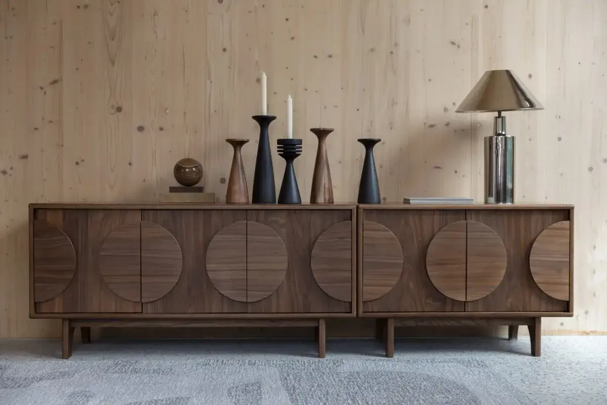 En skänk i valnöt med cirkulära dörrar, dekorerad med ljusstakar och en lampa. Klassisk design som lyfter rummet.