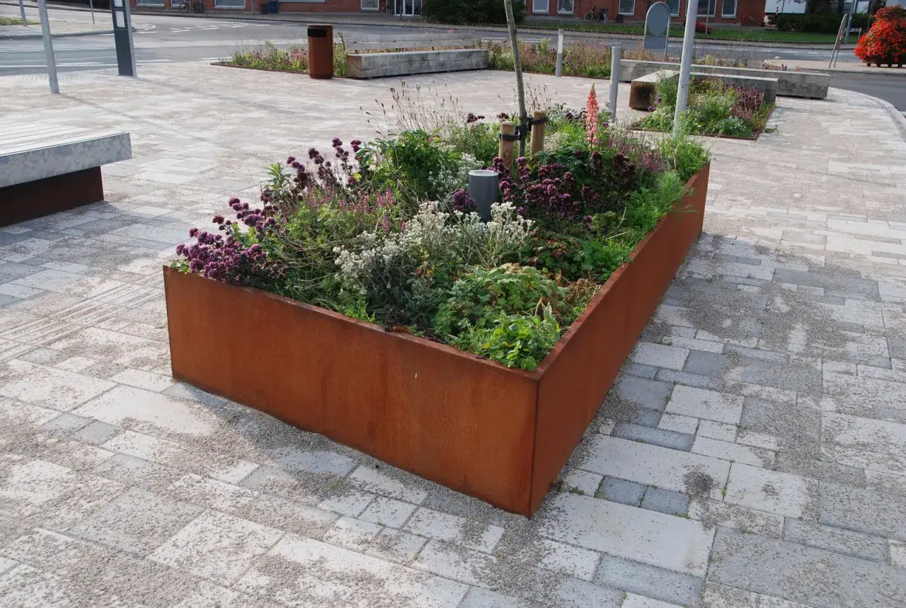 En rostig planteringsl&aring;da fylld med lila och vita blommor ger plantering inspiration i en stadsmilj&ouml;.