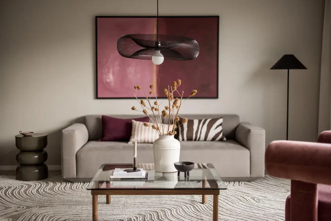 Ett mysigt tv-rum med en grå soffa, en stor tavla med rosa toner och en modern taklampa. Ett soffbord med en vas och torkade blommor skapar en inbjudande atmosfär.