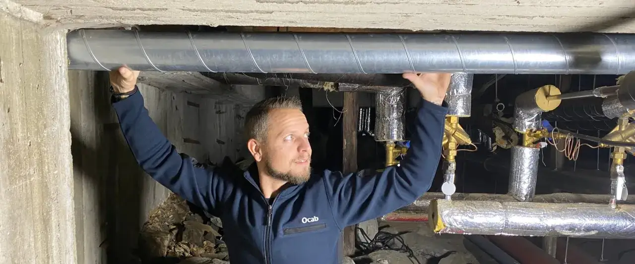 Man inspekterar rörsystem i krypgrund. Han håller i ett stort metallrör, en viktig del när man ska besiktiga hus.