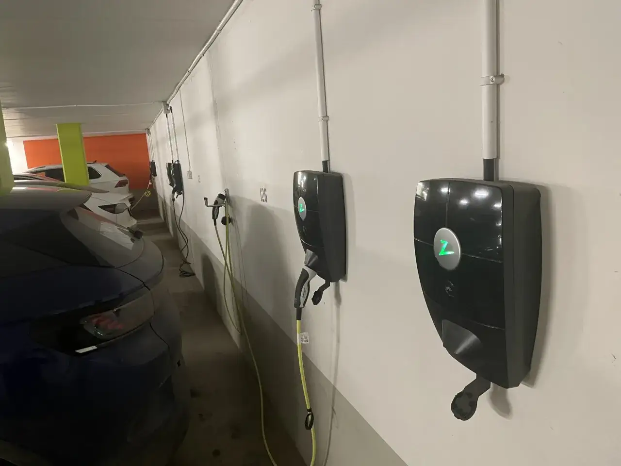Flera laddstolpar f&ouml;r elbilar i ett garage. En bl&aring; elbil syns i f&ouml;rgrunden. Brf:en har satsat p&aring; bidrag f&ouml;r laddstolpar.
