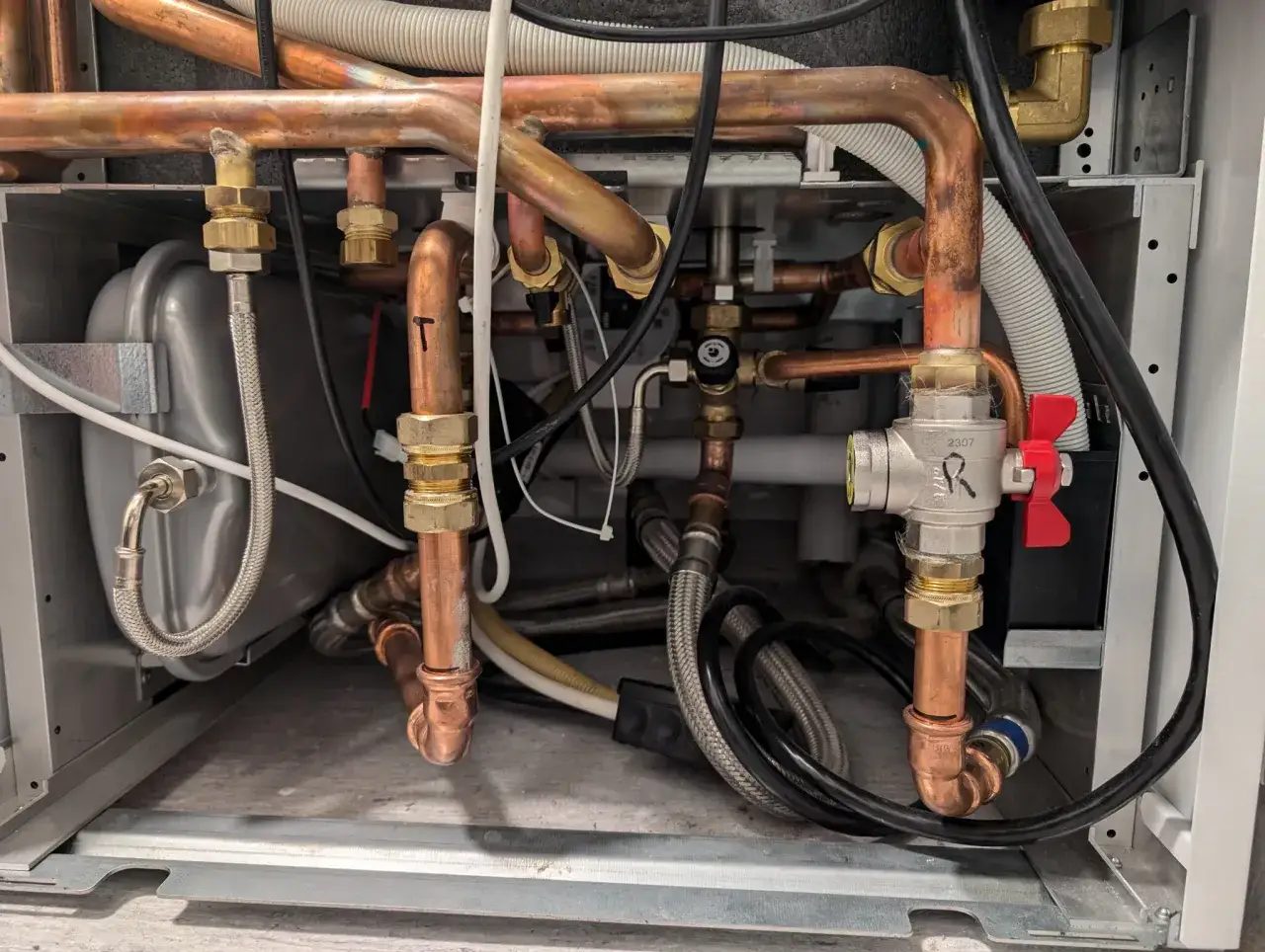 Detaljerad vy av rördragning och komponenter i en Bosch Compress 3800i EW9 värmepump. Kopparrör, ventiler och slangar syns tydligt.
