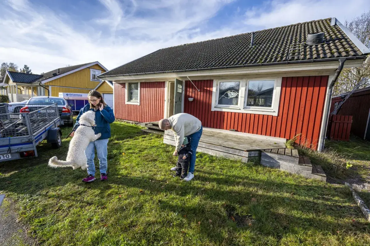 Familj med hund utanför rött hus. Kanske ett hus som ska säljas via kronofogden auktion hus.